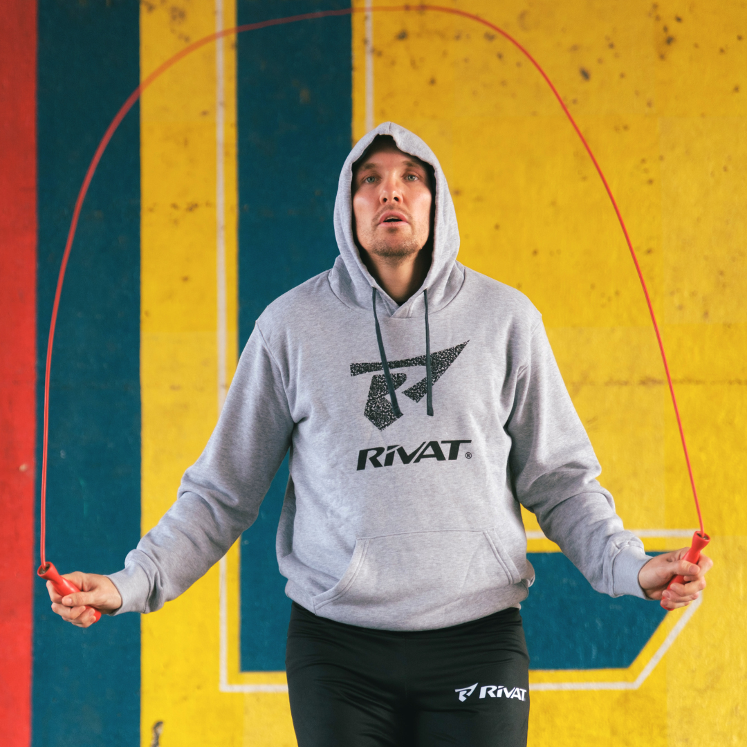 Homme en sweat à capuche faisant de la corde à sauter pour préparation physique boxe dans une salle colorée