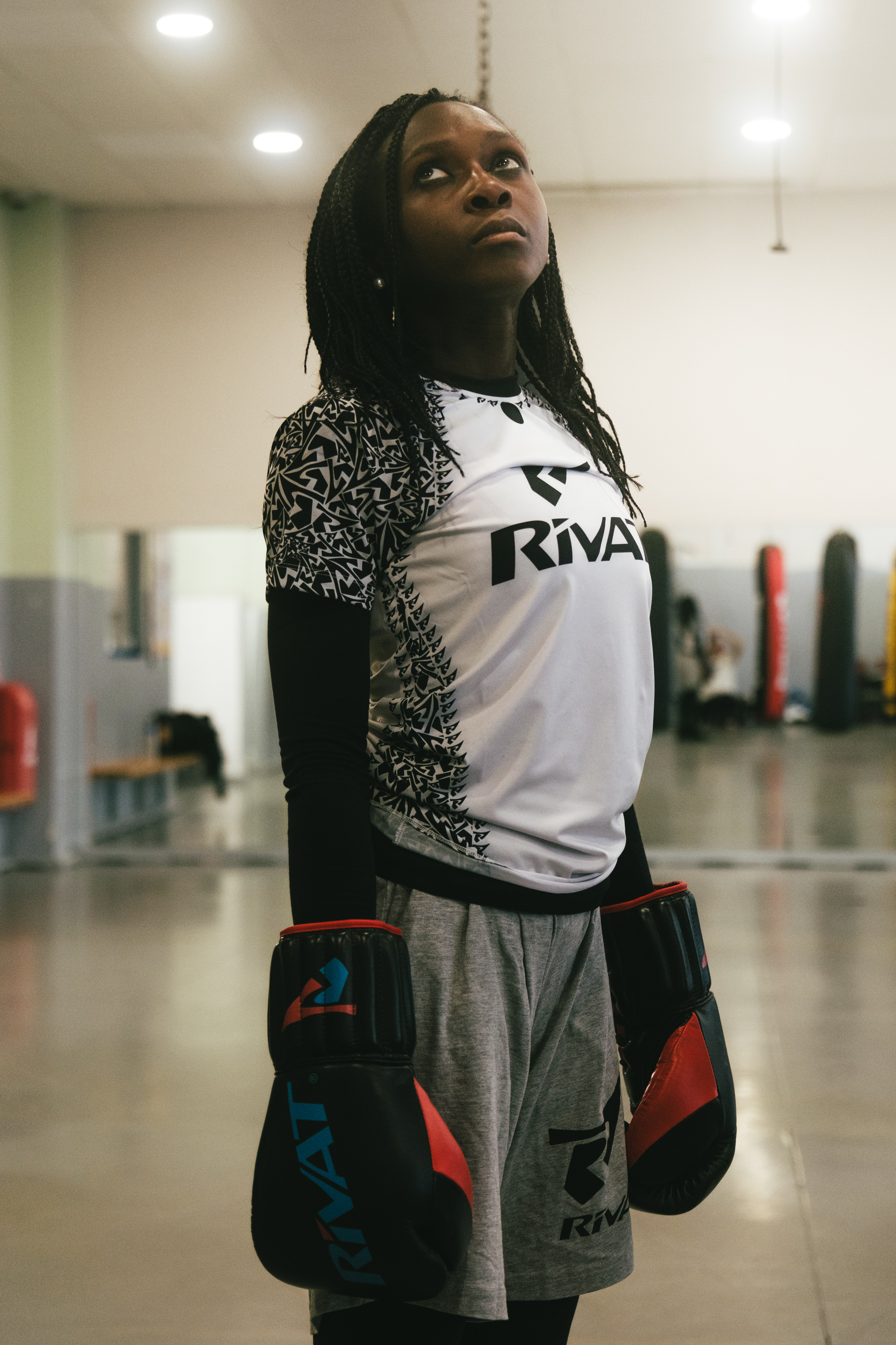 Femme portant une tenue boxe française Rivat avec gants et short dans une salle d'entraînement