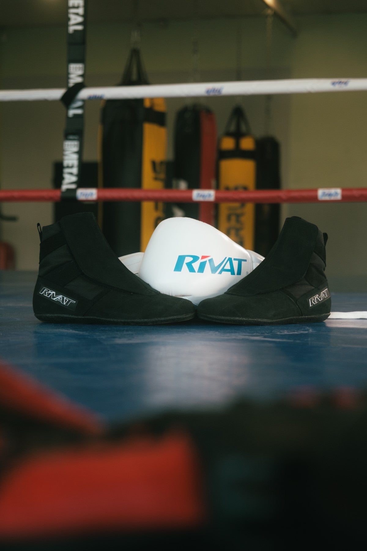 Chaussures boxe française noires posées dans un ring de boxe avec casque blanc Rivat