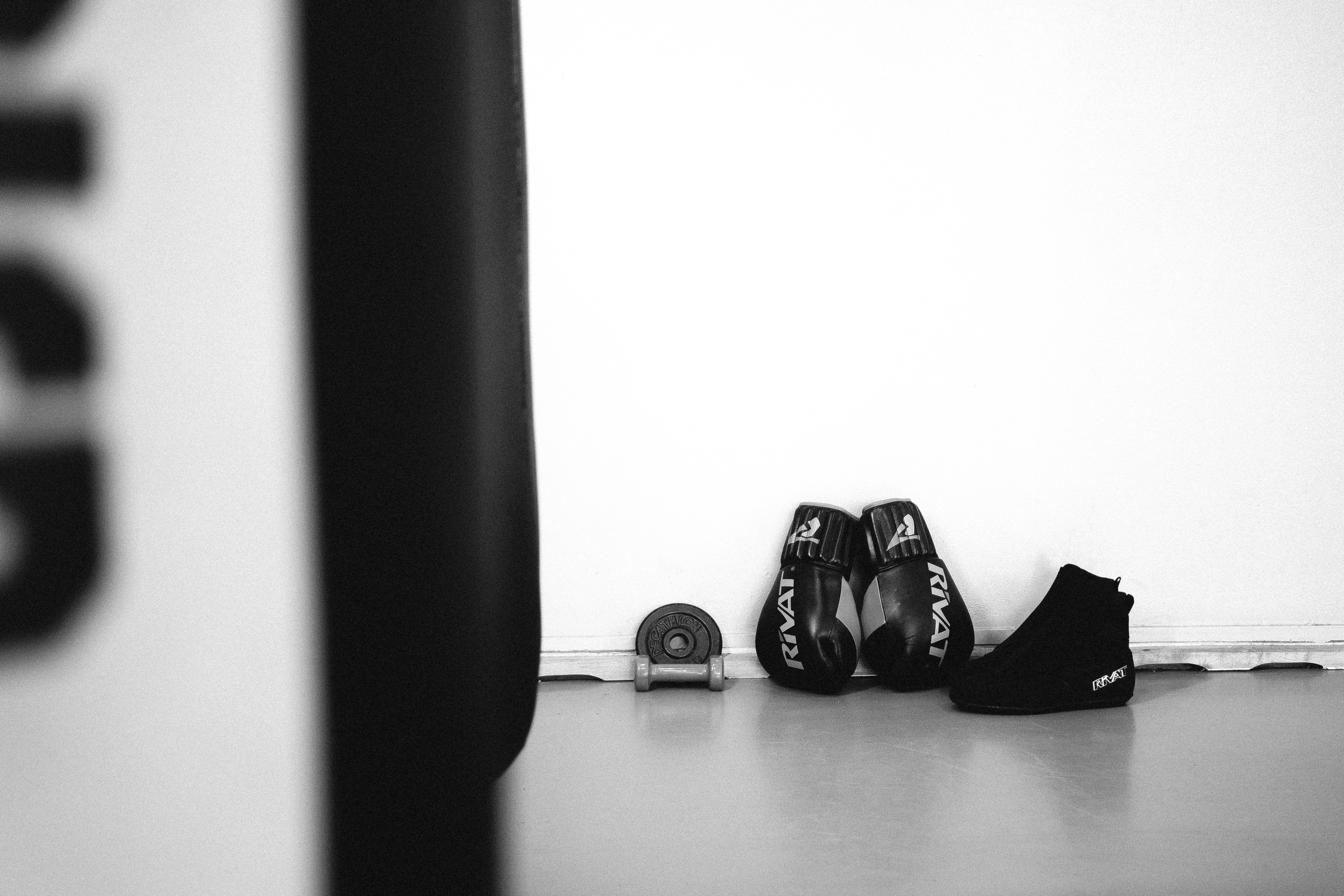 Chaussures boxe française débutant noires posées près d'un sac de frappe dans une salle d'entraînement