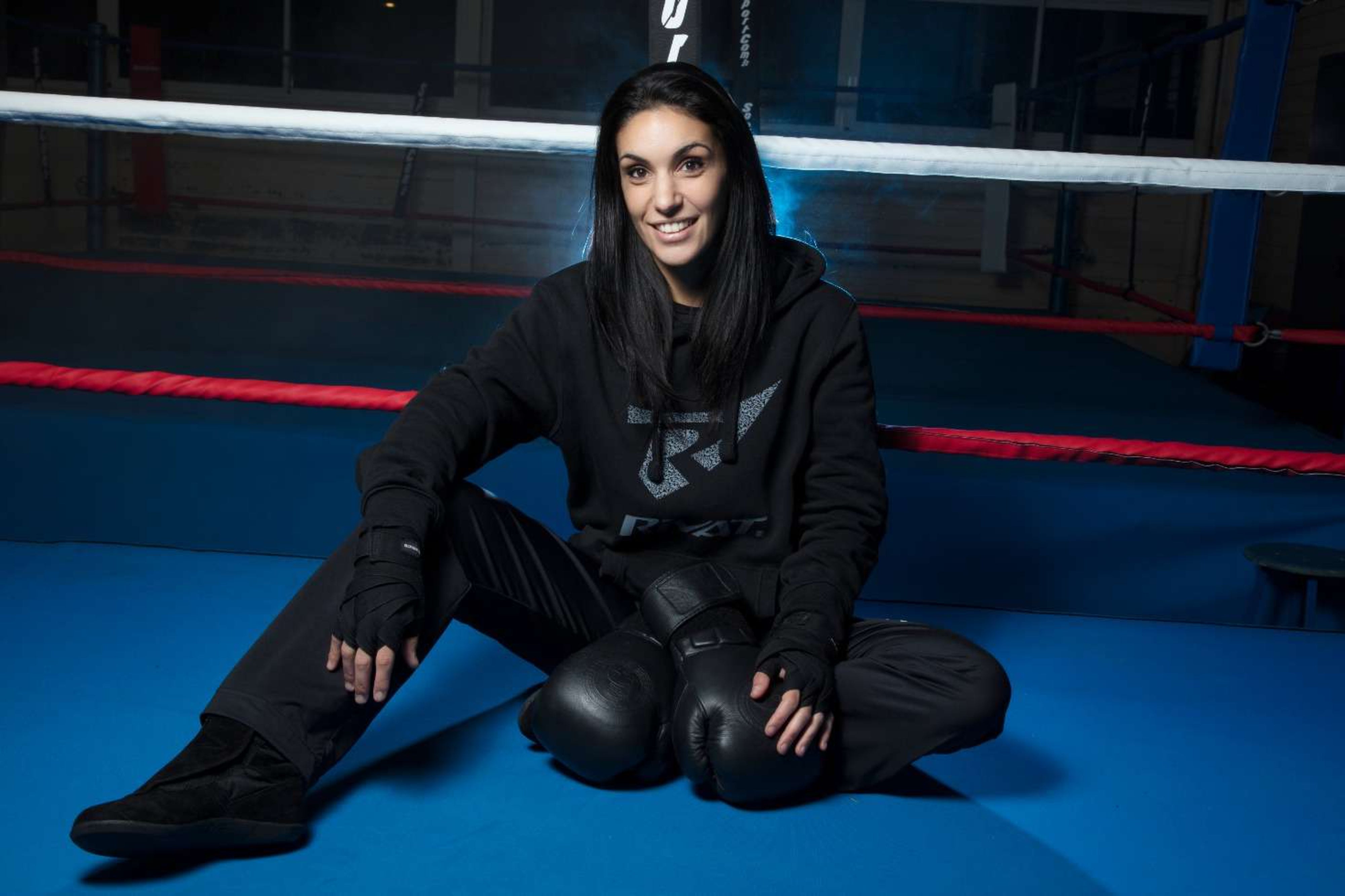 Femme assise dans un ring de boxe avec équipement boxe française femme noir et protections