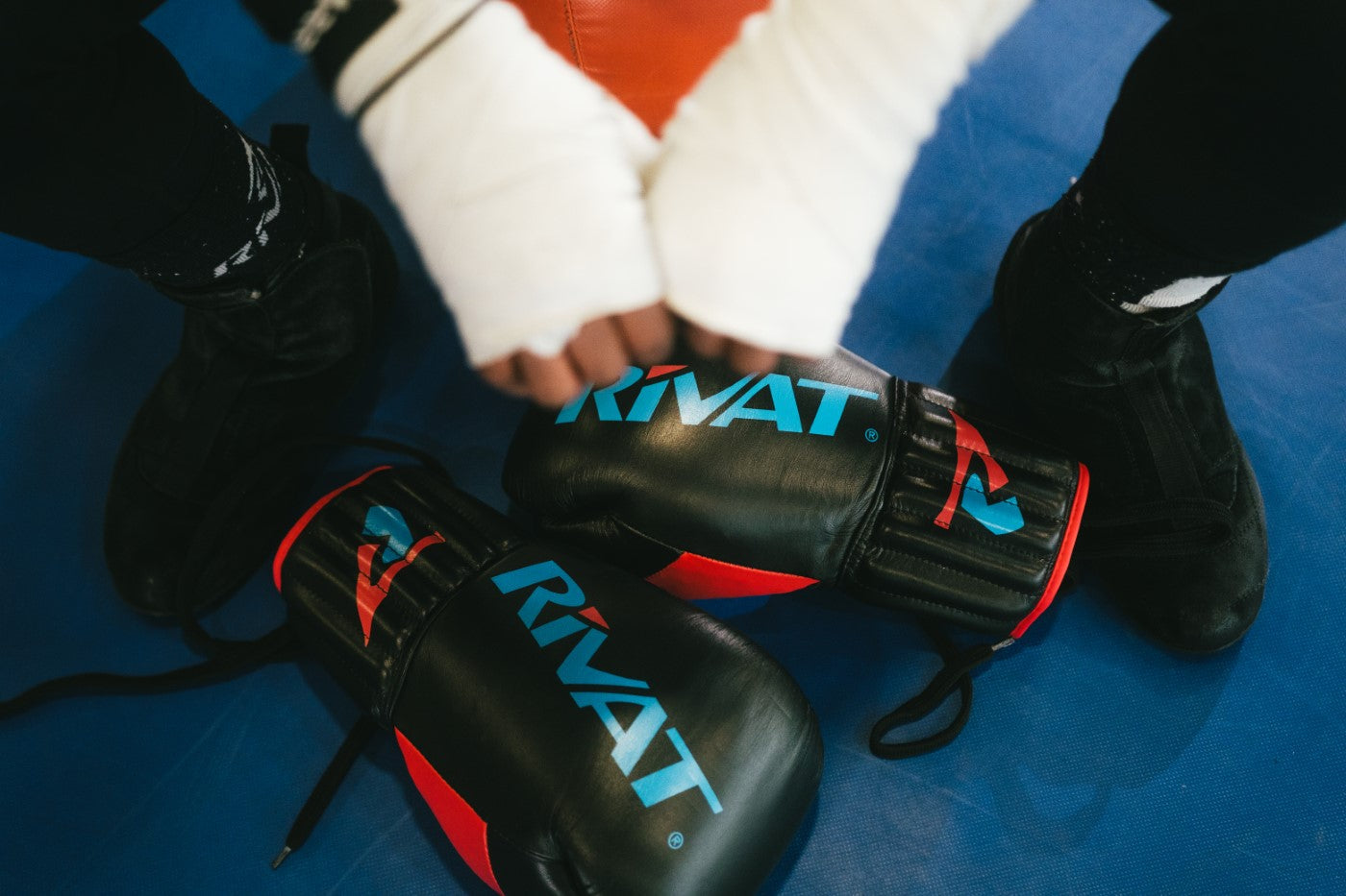 Gants de boxe Rivat posés sur un sol bleu avec mains bandées en préparation d'entraînement équipements boxe française