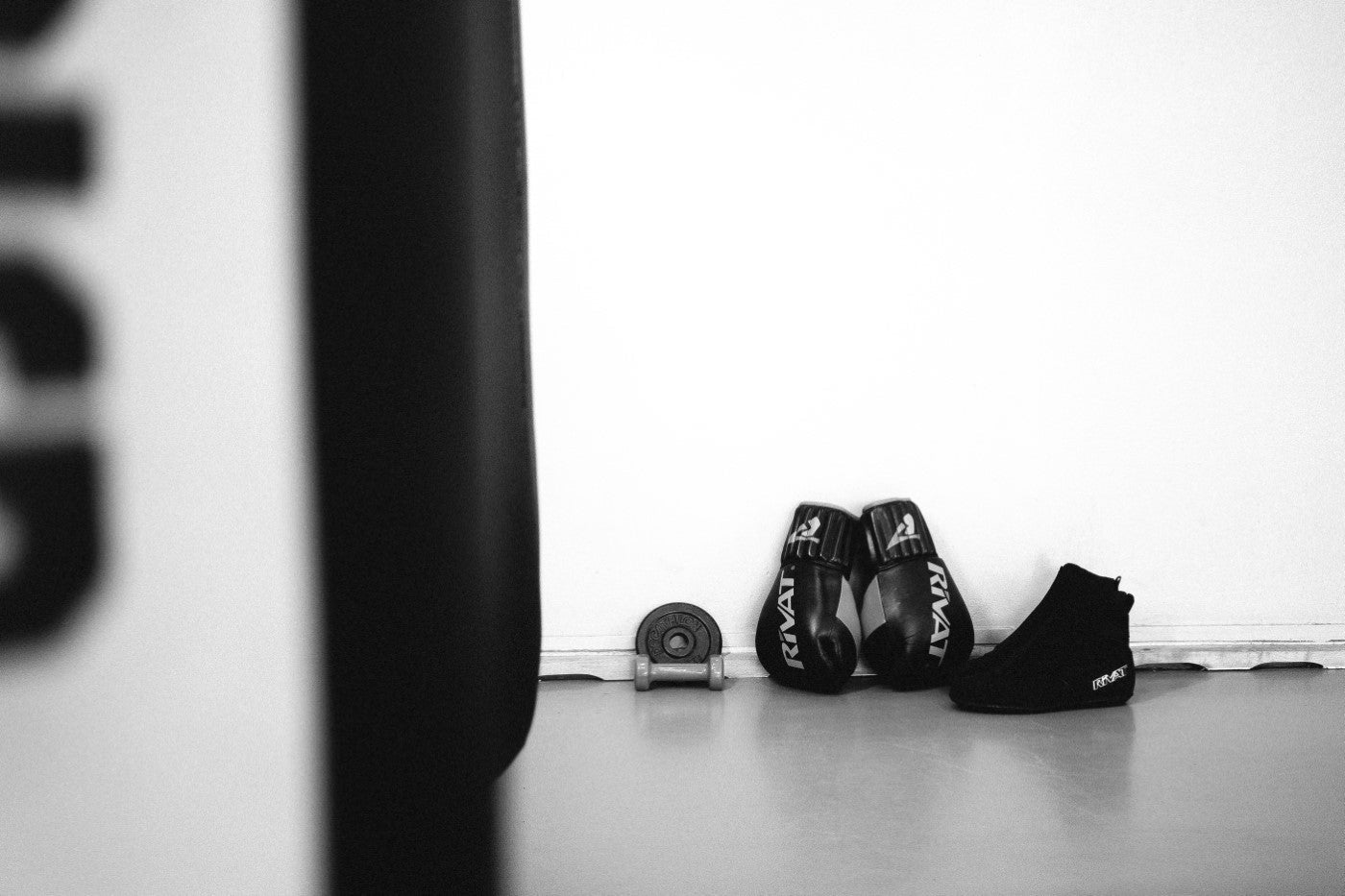 Chaussures boxe française compétiteurs noires RIVAT placées près d'un sac de frappe dans un espace d'entraînement