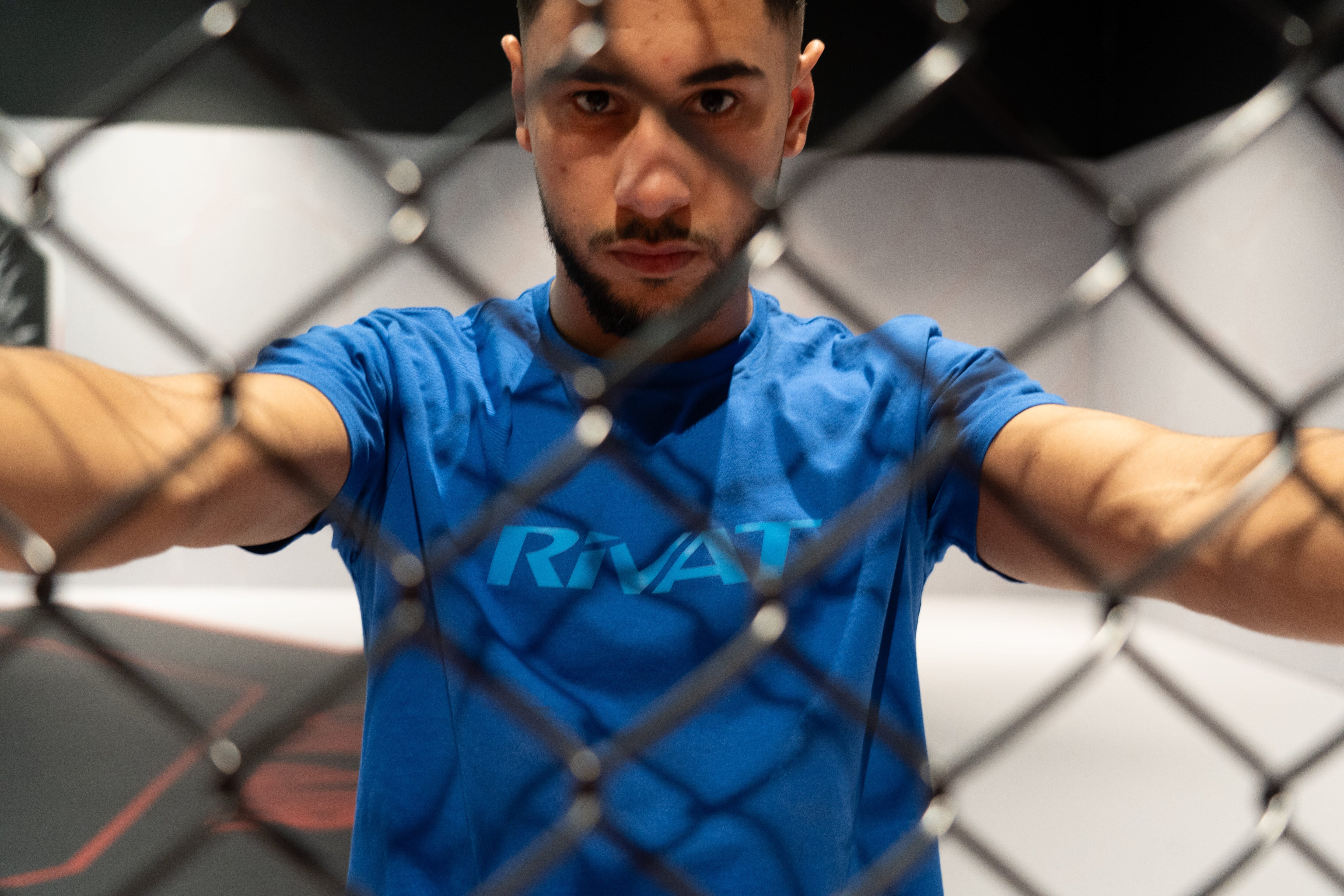 Homme portant un t-shirt bleu de la collection textile sport evo derrière une cage d'entraînement