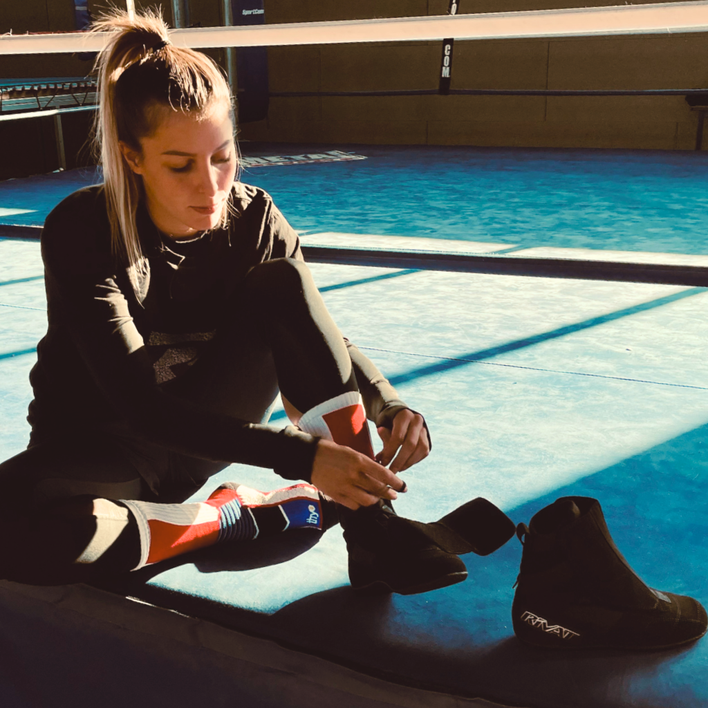 Femme en tenue de sport attachant ses chaussures de boxe dans un ring comment choisir chaussures boxe française