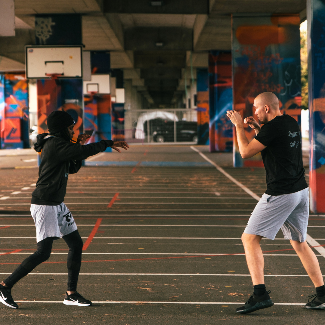 Deux pratiquants de boxe française s'entraînent en plein air pour maîtriser les techniques de base boxe française